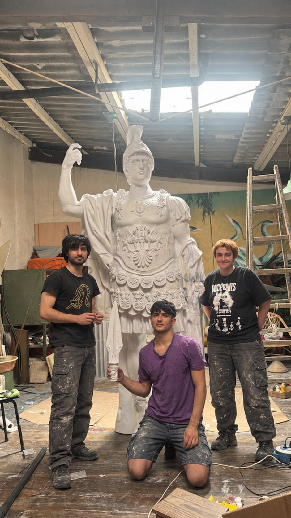 Tres personas junto a una estatua blanca en un taller